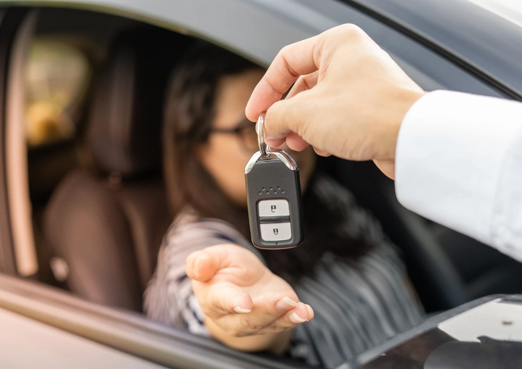 Rental desk agent handing car keys to a customer in the driver's seat